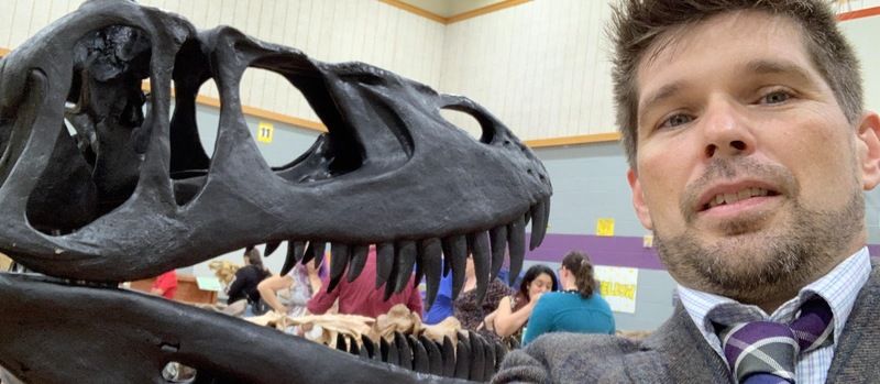 A school principal poses in front of a dinosaur exhibit