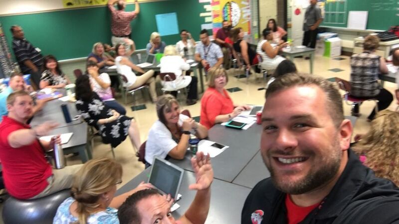 A teacher takes a selfie with other teachers at a faculty meeting