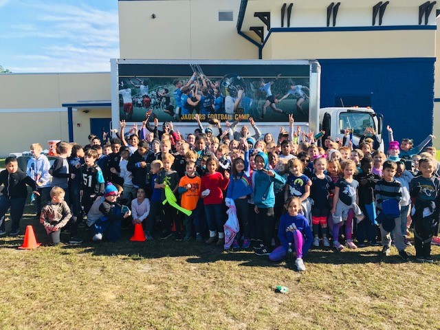 A photo of students who won a PBIS raffle in front of a truck with "Jaguars Football Camp" on the side