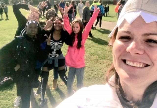 Principal in the foreground takes a selfie with students raising their hands in the background