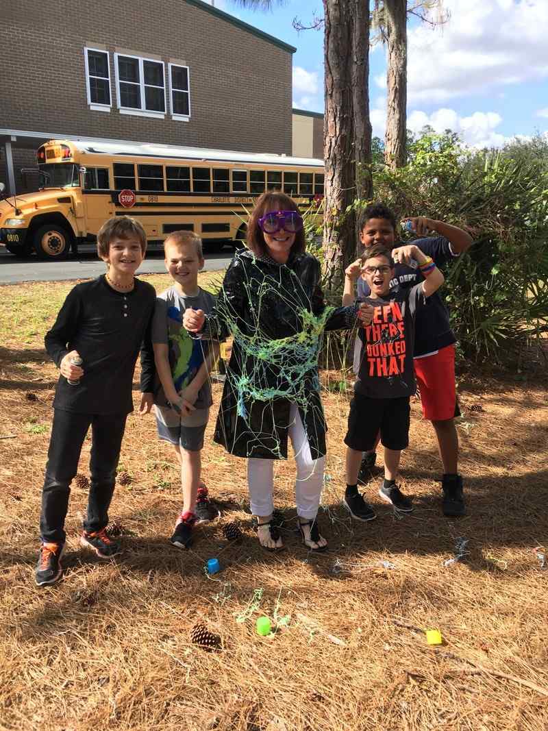 A principal wearing safety goggles and covered in silly string stands next to students