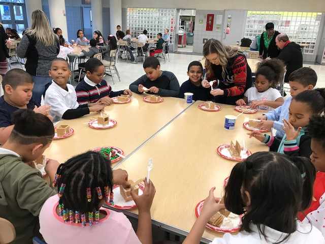 A group of students sit around a lunch table making gingerbread houses