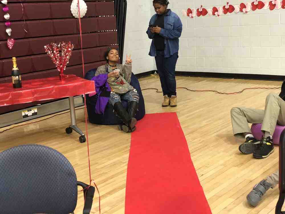 A student sits in a bean bag holding up a piece sign with a red carpet in front to show VIP section