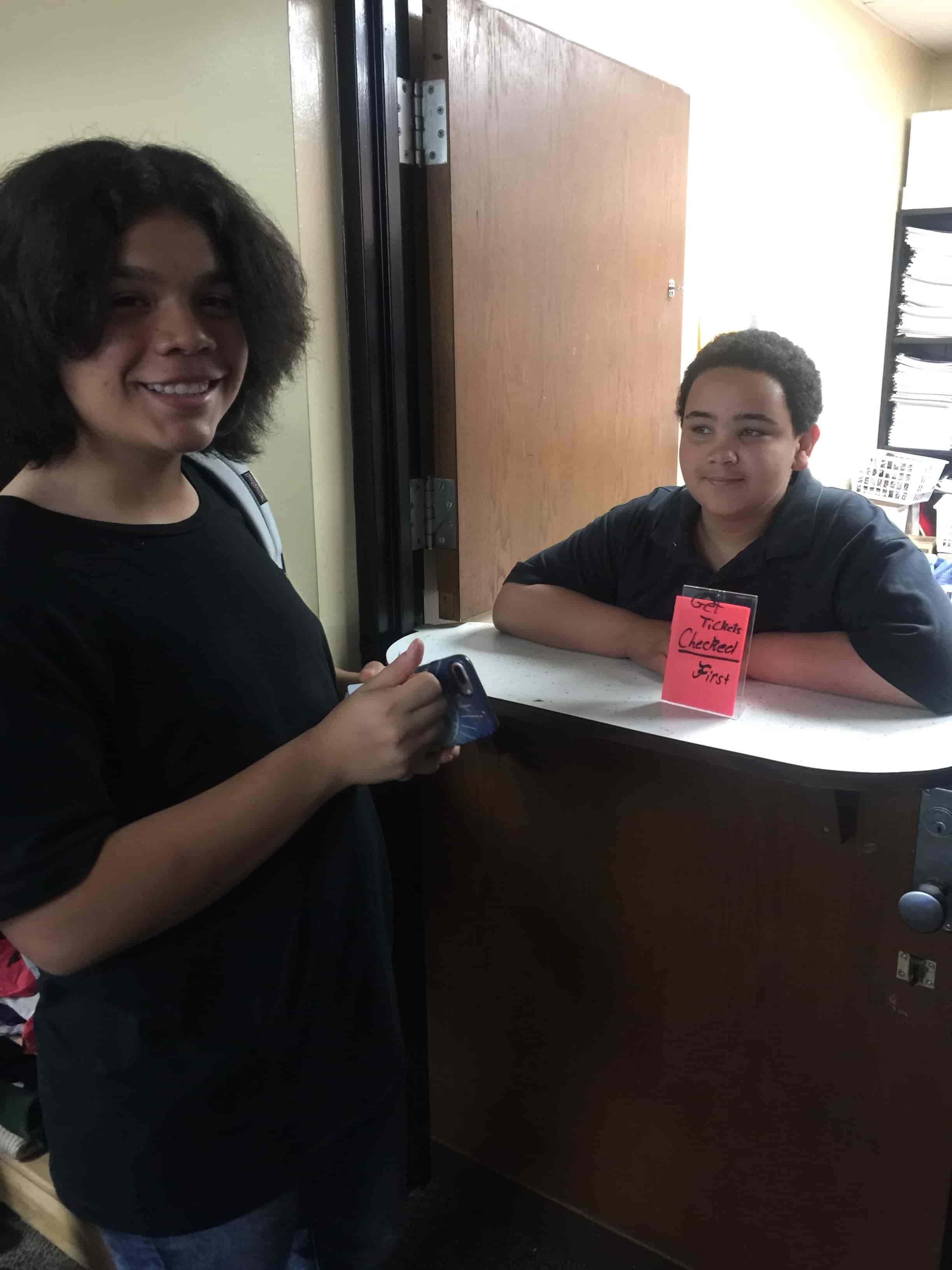 A student stands in front of a door as another student leads the school PBIS store