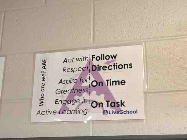 A piece of paper hangs in school hallway showing the school's AAE Acronym: Act with respect, aspire for greatness, Engage in active learning